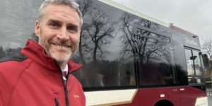 Gregor MIller, a Lothian Buses driver, stands beside a single deck city bus in his bus driver uniform.