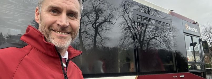 Gregor MIller, a Lothian Buses driver, stands beside a single deck city bus in his bus driver uniform.