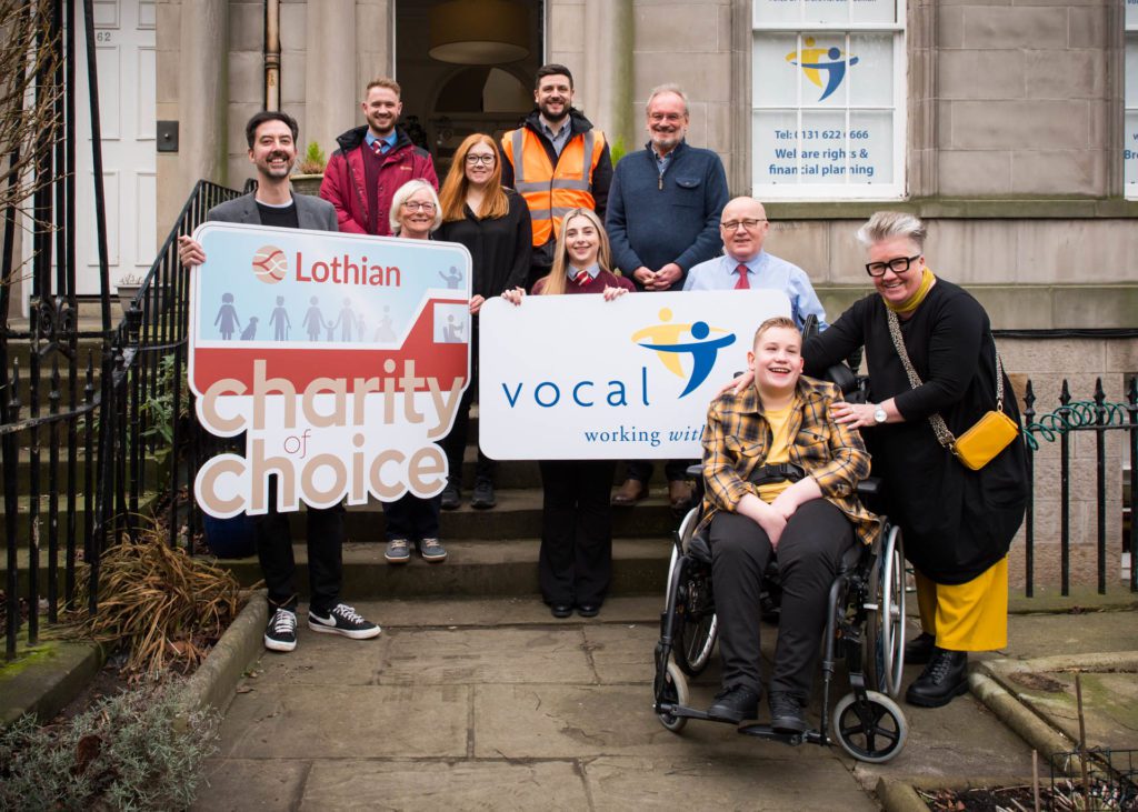 People from VOCAL and Lothian Buses stand of the steps of VOCAL's office for a photo, holding signs with their logos up.