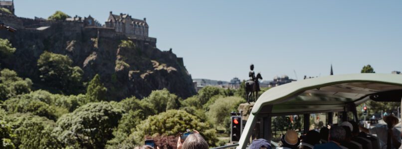 People on top deck of tour bus taking photos of Edinburgh Castle.