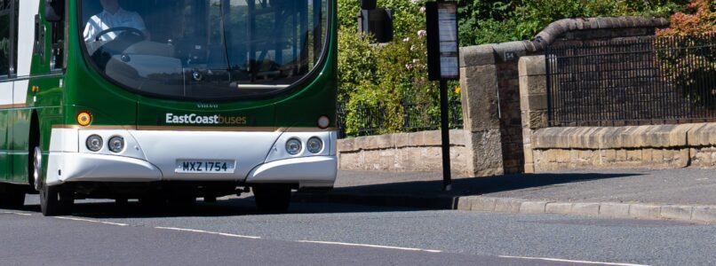 Image shows the front bumper of an East Coast bus beside a bus stop.