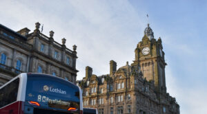 Image shows the top of a city bus with the Balmoral Hotel and clock in the background, set against a sunny blue sky.