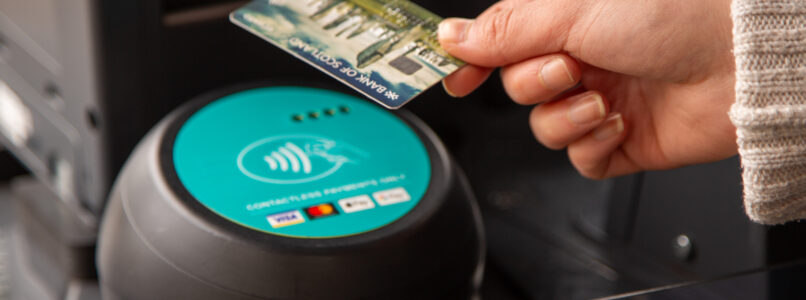 A hand holding a bank card taps it on the bus card reader.