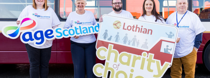Age Scotland staff stand in front of a Lothian bus holding signs for the charity and Lothian.