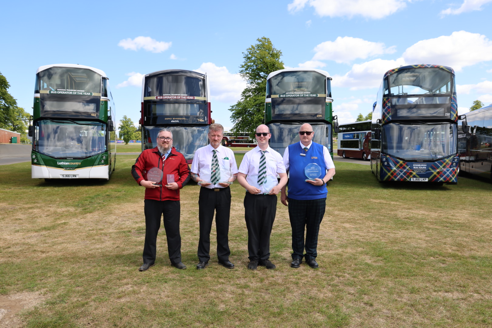 Four men holding trophies standing in front of the bus fleet.